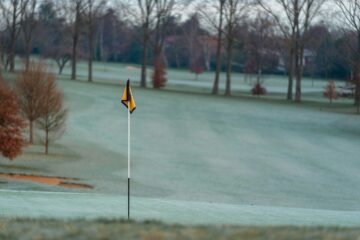 Frosttäckt golfbana med gulsvart flagga på greenen