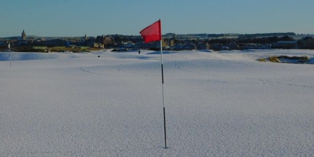 Röd golfbaneflagga står i ett vitt, frostigt landskap