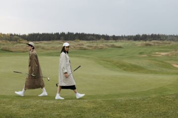 Två golfare går över fairway med klubborna i handen