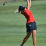 Golfspelare i röd tröja fullföljer en sving med drivern