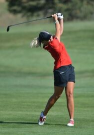 Golfspelare i röd tröja fullföljer en sving med drivern