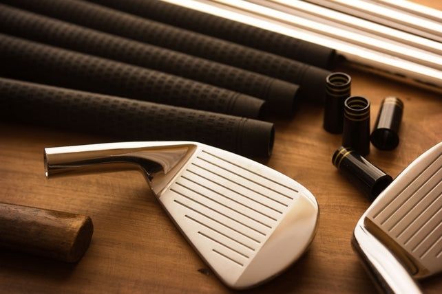 Olika golfklubbshuvuden och skaftdelar på ett träbord